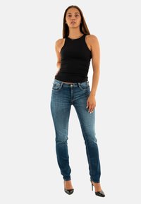 Top negro sin mangas combinado con jeans de mezclilla azules. Los jeans cuentan con bolsillos delanteros, un ligero desgastado y un diseño ajustado. Se llevan con tacones negros.