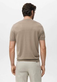 Suéter de punto beige de manga corta con cuello redondo, que presenta una textura suave y un diseño ajustado, combinado con pantalones de tono claro.