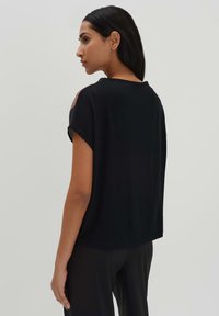 Top nero a maniche corte con vestibilità rilassata, caratterizzato da un collo rotondo e dettagli cut-out sulle spalle. Tessuto dalla texture liscia.