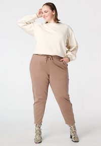 Beige sweatshirt met getextureerde mouwen, bruine broek met trekkoord en laarzen met slangenhuidpatroon. Eenvoudig ontwerp met een losse pasvorm.