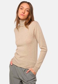 Pull col roulé beige à manches longues, en matériau doux, avec un design ajusté et des poignets et un ourlet côtelés.
