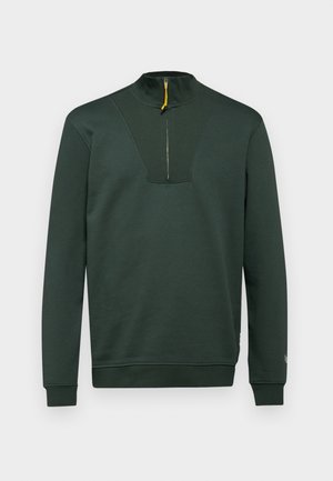 Ciemnozielona bluza z wysokim kołnierzem, połowicznym zamkiem błyskawicznym z żółtą pętelką oraz żeberkowymi akcentami na klatce piersiowej i mankietach. Gładka tekstura.