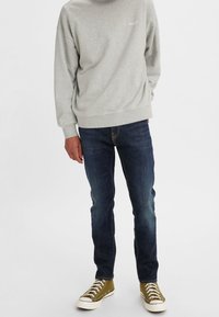 Sudadera gris de cuello redondo con logo, jeans de mezclilla azul y zapatillas altas verde oliva con suelas y cordones blancos.