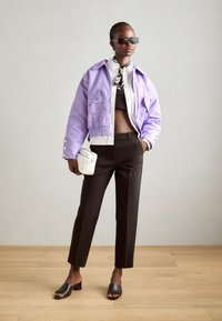Fialová zkrácená bunda, černý crop top, přizpůsobené černé kalhoty a černé mule. Doplněno bílou taškou a slunečními brýlemi.