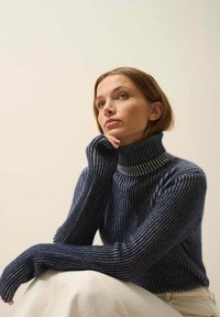 Marineblaues geripptes Rollkragensweatshirt mit kontrastierenden hellen Streifen, langen Ärmeln und strukturiertem Gewebe, kombiniert mit cremefarbenen Hosen.