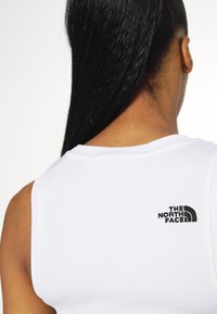 White sleeveless top with ribbed texture, featuring a black "The North Face" logo on the back. Smooth fabric with a slight sheen.