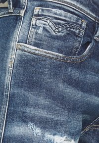 Blå denimjeans med en sliten finish, med en bakficka, sömnadsdetaljer och knäppning.