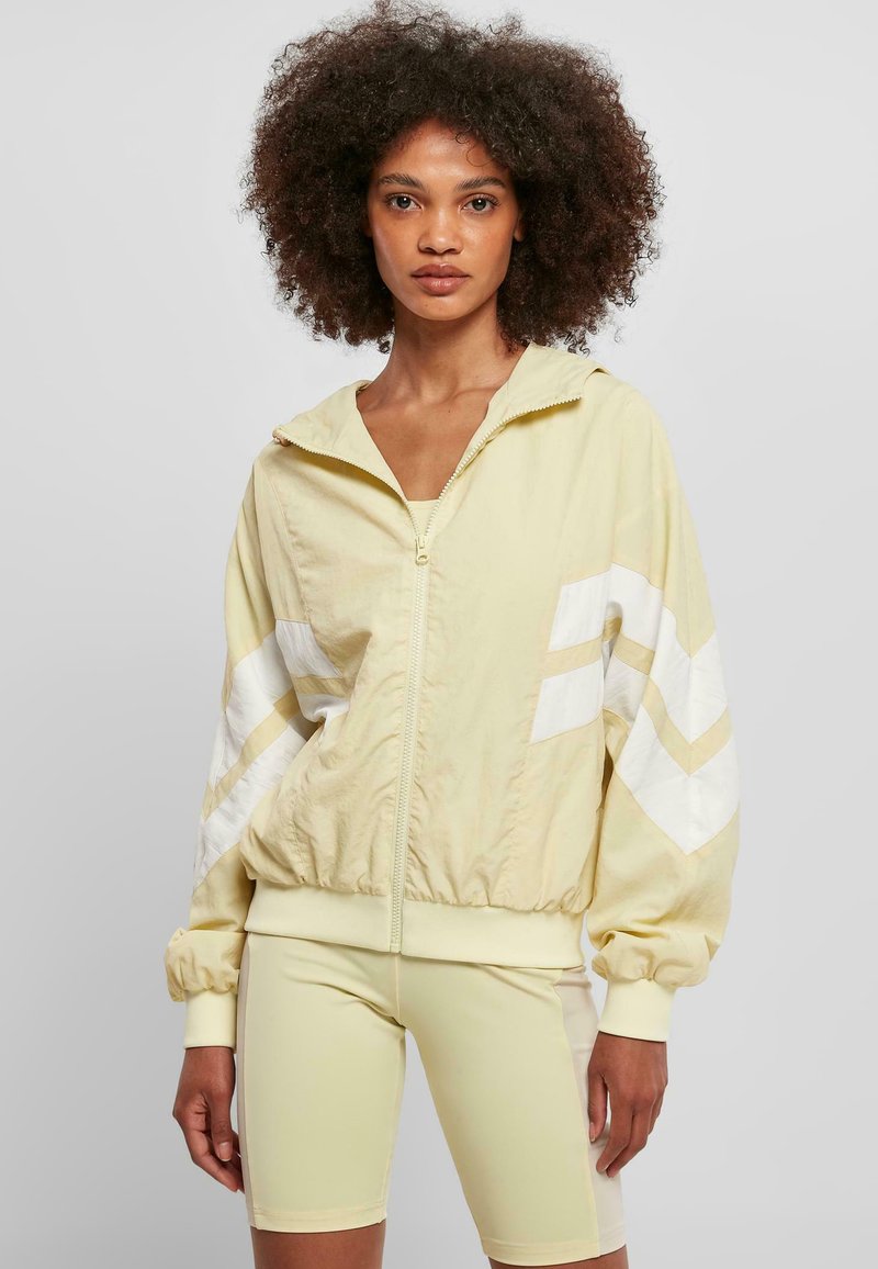 Ljusgul zip-up jacka med huva, prydd med vita chevronränder på ärmarna. Designad med en gatherad nederkant och mjuk textur.