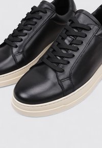 Baskets en cuir noir avec une finition lisse, dotées de lacets noirs, d'un bout arrondi et d'une semelle en caoutchouc couleur crème.