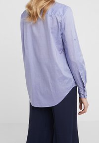 Camicia a maniche lunghe viola chiaro realizzata in tessuto morbido, con orlo arrotondato, polsini con bottoni e dettaglio della yoke sul retro.