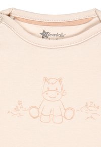 Hellbeige Babyshirt mit Rundhalsausschnitt, verziert mit einer sanften, hellorangen Illustration eines lächelnden Pferdes und Details von Gras.