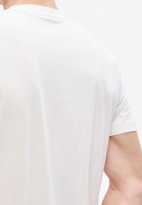 Λευκό T-shirt με κον�τά μανίκια από ελαφρύ ύφασμα, με στρογγυλή λαιμόκοψη και λεία υφή χωρίς ορατά μοτίβα ή γραφικά.