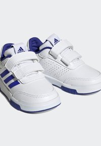 Zapatillas deportivas blancas con acentos azules, con dos correas de Velcro, lados perforados y suela de goma. Diseñadas para comodidad y soporte.