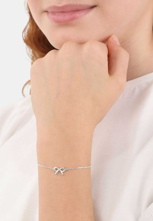 Silberne Kettenarmband mit einem kleinen Schleifenakzent. Die Kette ist zart und hat eine glatte Textur, getragen an einem Handgelenk vor einem hellen Hintergrund.