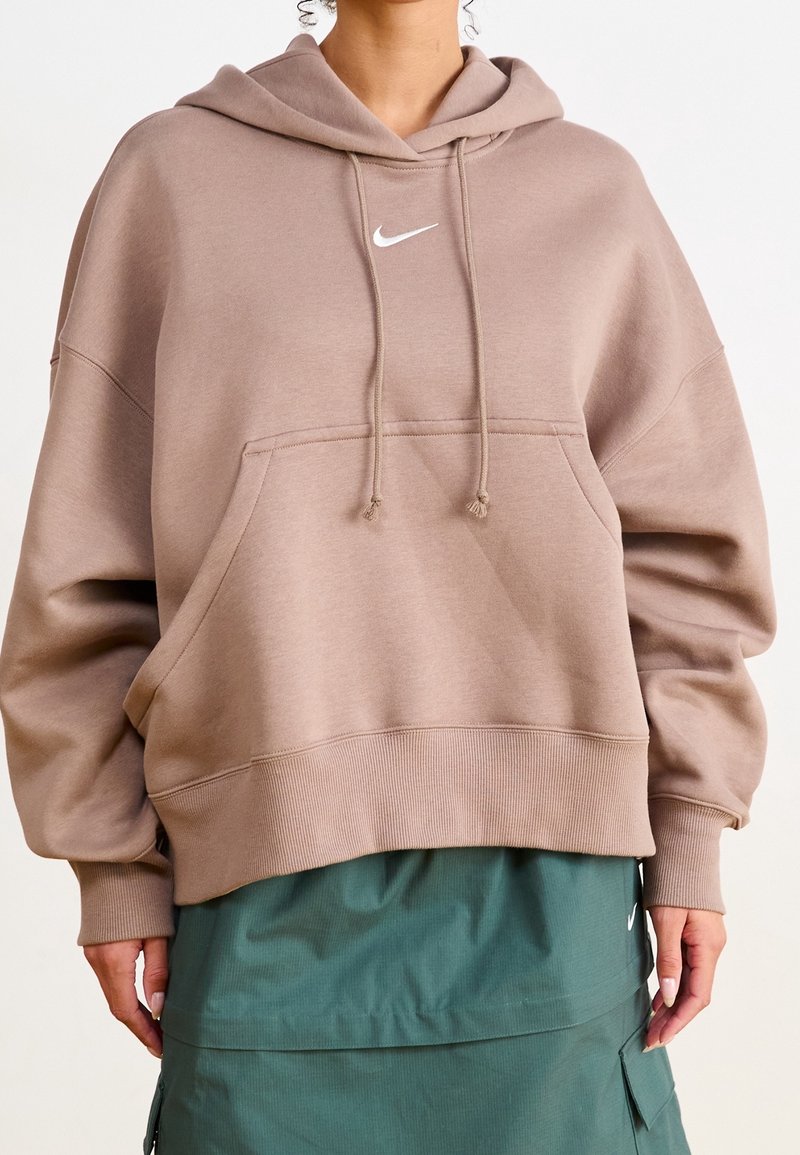 Person som bär en överdimensionerad mauve Nike-hoodie med framficka och dragsko, tillsammans med en grön lagerkjol med fickor.
