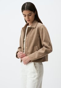 Veste courte en mélange de laine de couleur marron clair, avec un col, des fermetures à boutons et des poches latérales ; texture lisse.