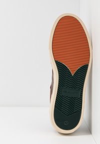 Brun skosål med et orange og grønt gummimønster, der har en fiskebensstruktur og GANT-logoet. Størrelse 42 vises.
