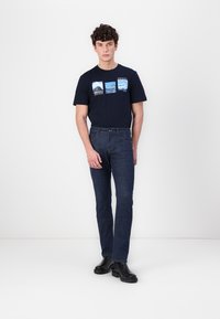 Marine crew-neck t-shirt met bedrukte landschappen aan de voorkant; gecombineerd met donkerdenim jeans en zwarte enkelboots. Eenvoudige, casual outfit.