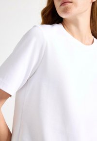 Hvid bomulds t-shirt med korte ærmer, rund halsudskæring og en afslappet pasform. Stoffet ser glat og blødt ud.