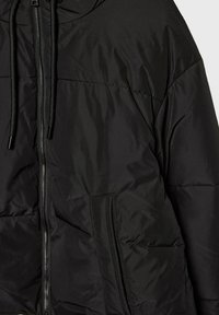 Doudoune noire avec capuche, dotée d'une fermeture éclair sur toute la longueur, d'accents avec cordons de serrage, d'une texture matelassée et de poches latérales.