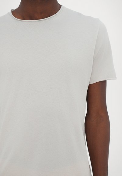 Camiseta de corte corto de color gris claro con mangas cortas, hecha de una tela suave, que presenta un cuello redondo y una textura lisa con sutiles detalles de costura.