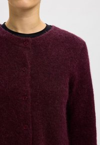 Mörk bordeauxfärgad cardigan i ett textured, mjukt material med rund halsringning och fem knappar framtill.