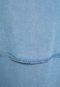 Tissu en denim bleu clair avec une texture lisse. Présente une couture courbée au bas avec un subtil détail de couture.