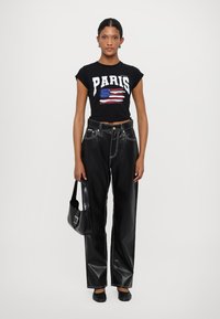 Black cropped t-shirt with "PARIS" graphic and flag design; high-waisted black faux leather pants; black flat shoes; small black handbag.