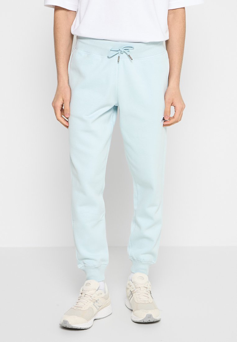 Pantalons de survêtement bleu clair en tissu doux. Dispose d'une taille à cordon de serrage et de poignets côtelés. Associés à des chaussures de sport beiges.