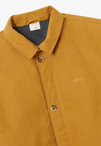 Μουσταρδί πουκάμισο με κουμπιά και γιακά, δύο ορατά κουμπιά, γκρι εσωτερική επένδυση και μικρό κεντημένο λογότυπο "Blkvis" στο στήθος.