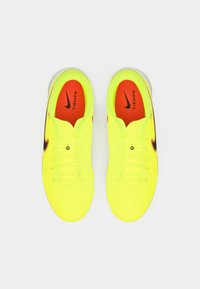 Botas de fútbol Nike Tiempo de color amarillo brillante con plantillas rojas y logotipos Swoosh negros, vista desde arriba sobre un fondo blanco.