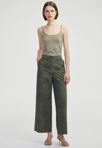 Grüne weite Hosen mit floralem Stickerei und Verzierungen, kombiniert mit einem enganliegenden beigen Tanktop. Die Stoffe wirken glatt und leicht.
