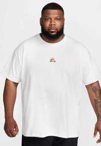 White short-sleeve t-shirt featuring a small orange and black logo on the chest. Made from cotton, it has a relaxed fit and smooth texture.