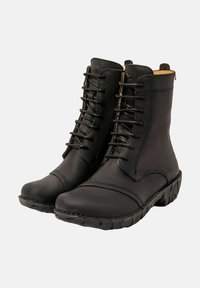 Un par de botas negras de cuero hasta el tobillo con cordones en la parte delantera y suelas de goma resistentes sobre un fondo gris.