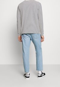 Randig långärmad skjorta i vitt och svart, i kombination med ljusblå jeans och svarta sneakers med vita sulor och Nike-logotyp.