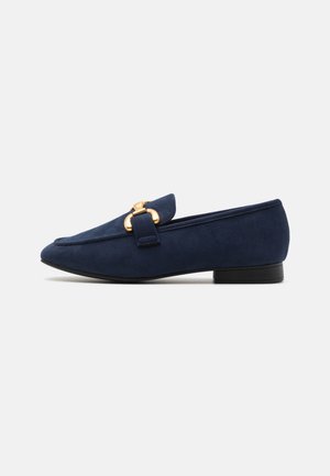 Marineblå ruskindslipper med lav sort hæl og guldfarvet metal hestebid detalje på toppen.