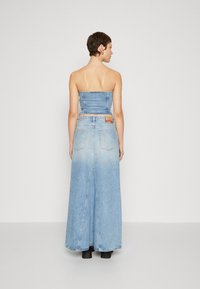 Robe maxi en denim avec un haut ajusté sans bretelles et une jupe évasée. Tissu bleu clair, décoloration subtile et poches à l'arrière.