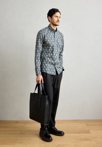 Tamsiai mėlyno ir žalio gėlių rašo marškiniai su mygtukais, derinami su juodomis kelnėmis ir elegantiška juoda rankine, nešiojami su juodais batais.