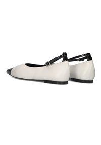 Platte schoenen met een witte leren bovenkant en een zwarte gepatineerde neus. Voorzien van een verstelbare zwarte band met een zilveren gesp.