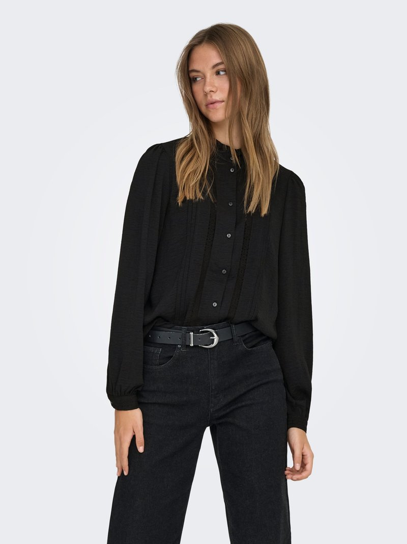 Svart skjorta med knappar och långa ärmar, i ett subtilt texturerat tyg med vertikala veck och ett smalt svart bälte med ett silverfärgat spänne.