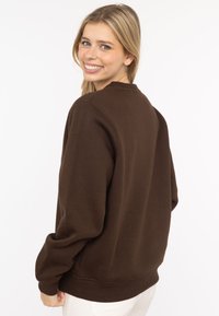 Brązowa bluza z miękkiego materiału, z długimi rękawami, okrągłym dekoltem oraz ściągaczami u rękawów i na dole. Prosty, jednokolorowy design.