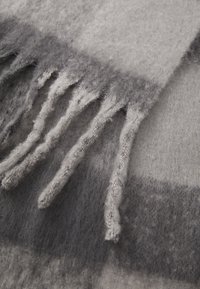 Cachecol de lã cinza com uma textura suave, detalhes em franjas e um padrão mesclado de tonalidades de cinza escuras e claras.