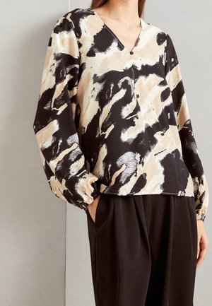 Blouse à manches longues et col en V dans un motif aquarelle noir, beige et crème, avec des détails de boutons et des poignets froncés, portée avec un pantalon noir.