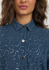 Camicia in denim con motivo a spina di pesce, decorata con paillettes argentate, colletto e chiusura a bottoni a pressione, di colore blu scuro.