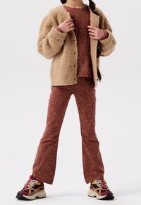 Beige fuzzy cardigan over a red speckled top and matching flared pants, paired with multicolored chunky sneakers.