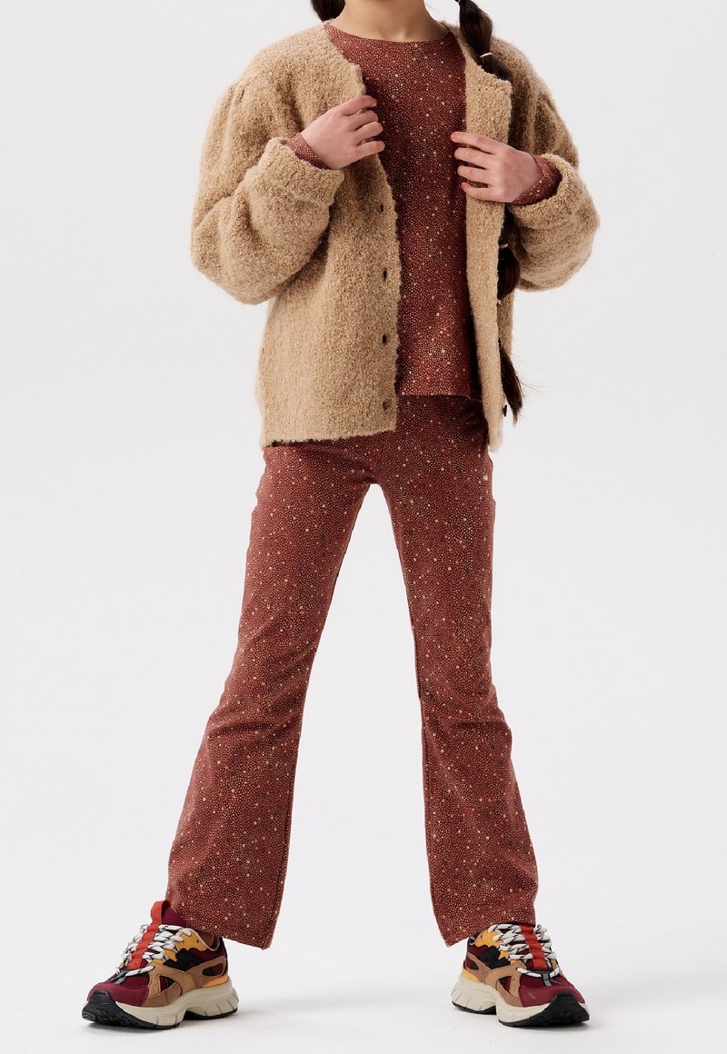 Beige fuzzy cardigan over a red speckled top and matching flared pants, paired with multicolored chunky sneakers.
