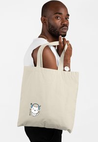Borsa tote in tela beige con due manici robusti, caratterizzata da un gatto da cartone animato con cuffie e note musicali stampate sul davanti.