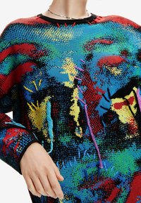 Pull en tricot coloré avec un motif abstrait multicolore incluant du rouge, du bleu, du jaune et du noir. Comprend des coutures décoratives dans diverses couleurs.