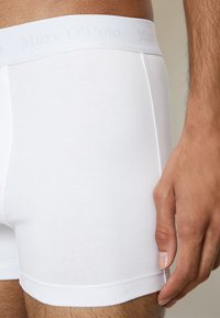 Boxer in cotone bianco con una morbida fascia elastica e logo in rilievo. Tessuto liscio, forma aderente e lunghezza a metà coscia.