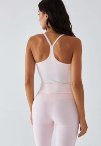 Jasnoróżowy sportowy tank top o dopasowanym kroju z ramiączkami typu racerback, zestawiony z dopasowanymi legginsami o gładkiej fakturze i bezszwowym wykończeniu.